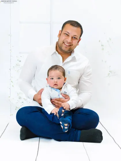 A heartwarming father and son portrait against a clean white backdrop. The father's gentle smile and the baby's curious gaze make this a special memory.