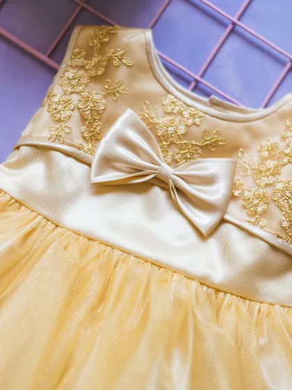This golden-yellow dress features beautiful floral embroidery on the bodice. A simple satin bow at the waist completes this elegant and cheerful design.