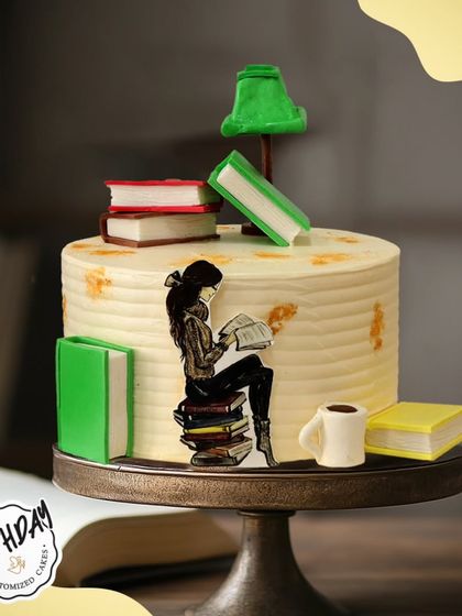 A perfect cake for a book lover. This design features a fondant figure reading on a stack of books, complete with a lamp and a cup of coffee.