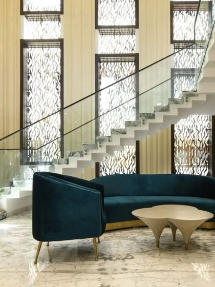 This living area is designed for connection, featuring a deep blue curved sofa that encourages conversation. The space is framed by a grand staircase and intricate window screens, blending modern comfort with detailed architectural elements.
