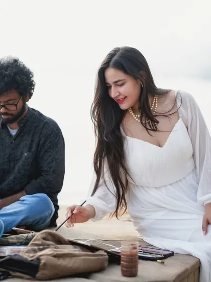 We can incorporate creative concepts into your pre-wedding shoot. Here, the bride-to-be tries her hand at painting by the ghats, adding a personal and artistic touch to their story.