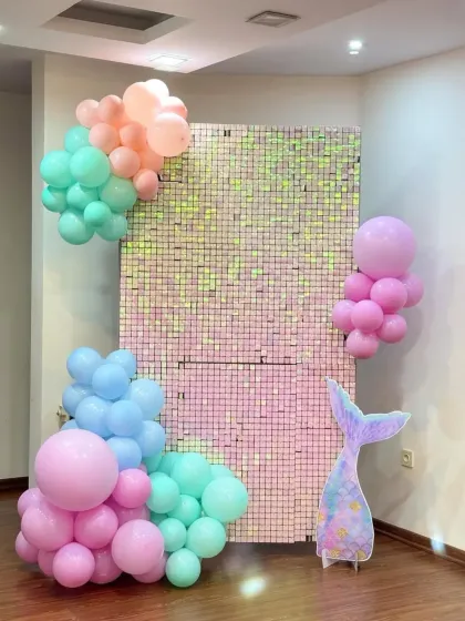 A minimal mermaid theme with pastel balloon clusters on a sequin wall and a mermaid tail cutout.