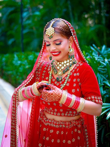 A happy bride in a vibrant red lehenga, shot outdoors to take advantage of the natural greenery.