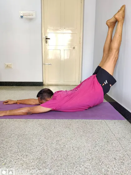 Viparita Shalabhasana (Inverted Locust Pose) with feet on the wall. This variation strengthens the back muscles and prepares the body for arm balances and deeper backbends.