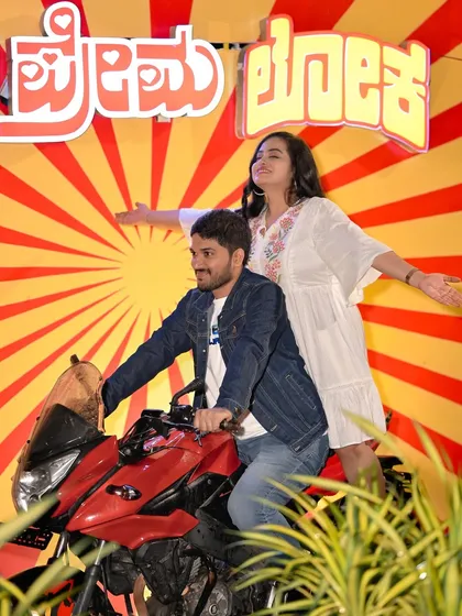 A fun, retro-style shot with our 'Premaloka' movie backdrop and a motorcycle, perfect for film-loving couples.
