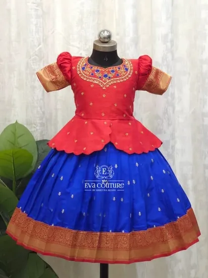 A classic Pattu Pavadai with a modern twist. This outfit features a bright red peplum top with delicate neck embroidery, paired with a royal blue silk skirt and a traditional zari border.
