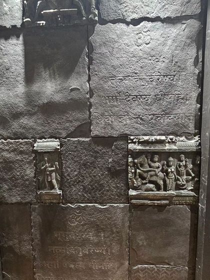 A feature wall made of dark stone panels with carved Sanskrit shlokas and religious figures, creating a powerful and spiritual ambiance.