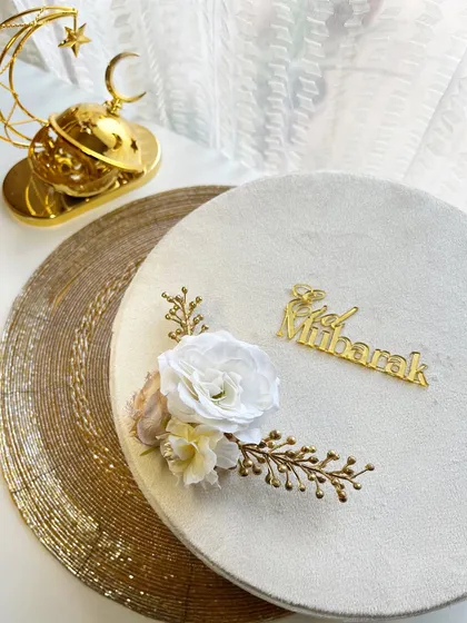 An elegant white velvet box decorated with floral accents and an "Eid Mubarak" sign, placed next to a golden crescent moon incense burner.