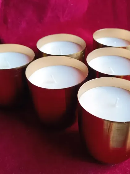 A set of six brass jar candles against a rich red background.