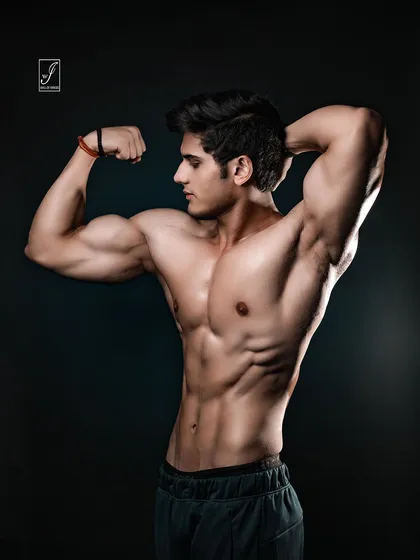 An alternate take on the classic bicep flex, captured from a profile angle to showcase the full curvature and size of the arm muscles. This is a testament to hard work and dedication in the gym.