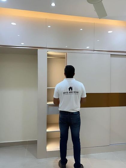 A full-height sliding wardrobe with a two-tone design in off-white and gold. The internal section features sensor-activated lights and a pull-out drawer for organized storage.