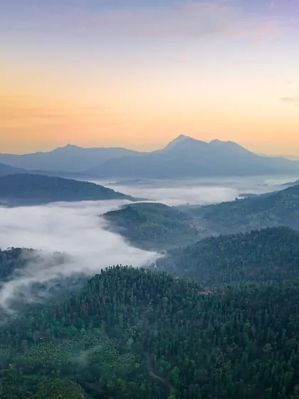 A breathtaking aerial view of the Western Ghats near Kalasa, with morning fog filling the valleys below the towering peaks.