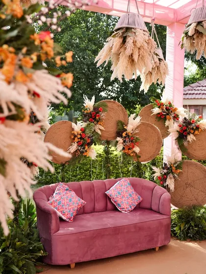 A close-up of the bride's seating, featuring a plush pink sofa and a backdrop of woven discs and pampas grass. This detail shot highlights the unique textures and materials I use in my designs.
