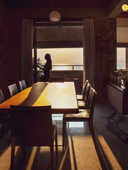 Golden hour at 'The Canvas' project in Marine Drive. The setting sun casts long shadows across the dining area, highlighting the texture of the exposed brick and the warmth of the wooden table, showcasing how light transforms a space throughout the day.