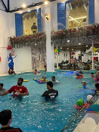 A wide shot of a busy pool party, showing adults and kids enjoying the water together under the festive party decorations.