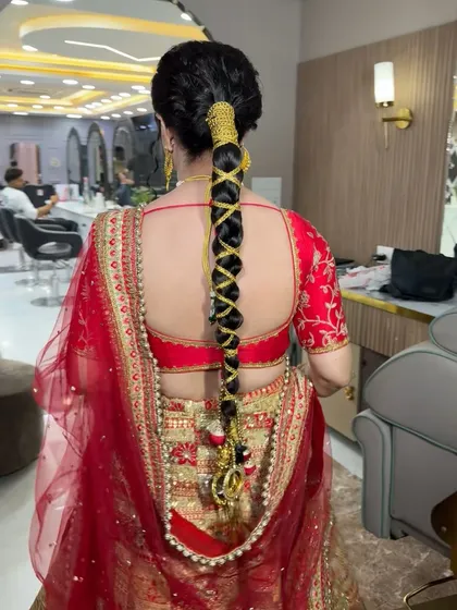 This is a great example of a traditional yet stylish bridal hairstyle. We created a long, intricate parandi braid, weaving in golden accessories to match her red and gold lehenga for a classic Punjabi bridal look.