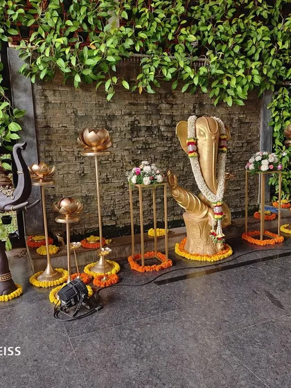 A sacred corner featuring a Ganesha idol, adorned with floral garlands and surrounded by traditional brass lamps and flower arrangements to welcome guests with blessings.
