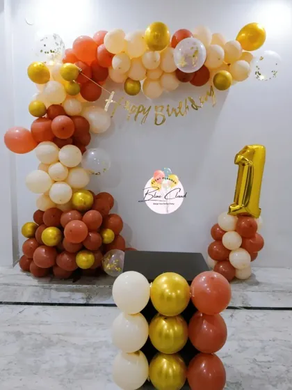 A simple L-shaped balloon arch in warm tones for a first birthday celebration at home.