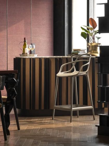 The bar area in the Caitriona apartment, featuring a standalone bar with a white onyx top and wallpaper-clad shutters. A playful Kartell bar chair adds a touch of modern design to this sophisticated entertaining space.