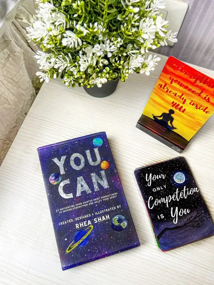 A cozy, lifestyle shot of motivational card decks on a bedside table with flowers. This helps customers imagine incorporating these products into their daily routines.
