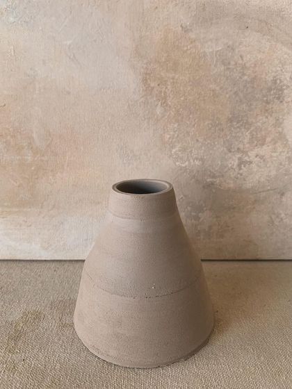 A raw, unglazed vase with a wider base, showing the beautiful, subtle texture of the clay.