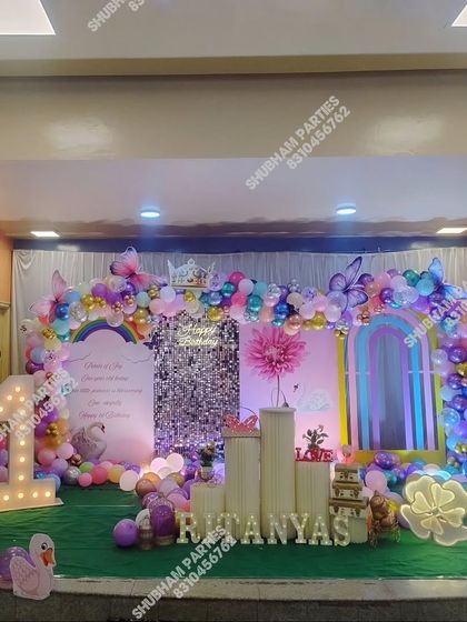 A grand stage decoration for a first birthday with a rainbow and swan theme.