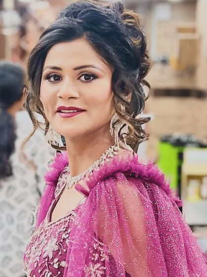 A vibrant party look featuring a magenta gown with dramatic ruffled sleeves. We styled her hair in an elegant updo and chose makeup with a bold lip to match the energy of the outfit.
