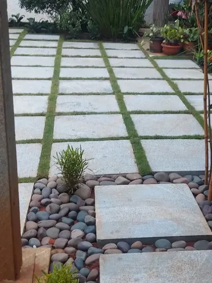 A large patio area created with square pavers and grass joints, surrounded by a pebble border. This design is both visually interesting and permeable, allowing rainwater to soak into the ground.