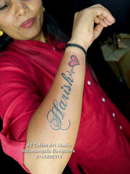 A "Harish" name tattoo in a beautiful script font with a heartbeat and initial.