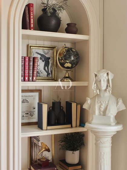 The shelves are styled with a curated collection of books, classical busts, and vintage objects like a globe and gramophone horn, telling a story of travel, knowledge, and history.