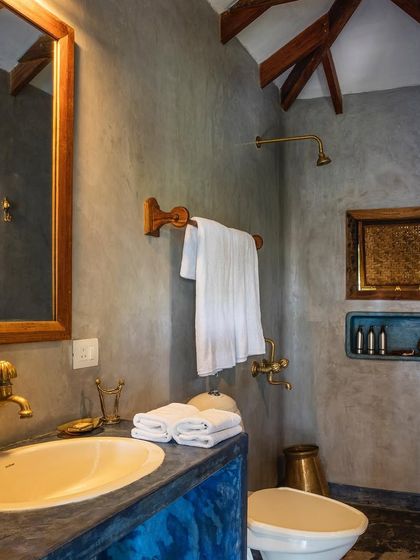 The bathroom of the Sky Room features indigo-dyed plaster walls and custom brass fittings. The design combines rustic textures with elegant details, creating a unique and luxurious bathing space.