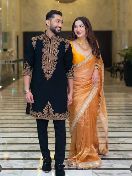 The complete look. Our black sherwani with detailed gold threadwork on the collar, placket, and cuffs, paired with tailored trousers for a sharp, regal silhouette.