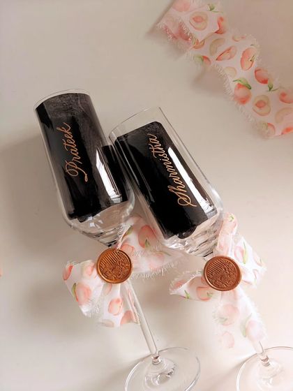 Calligraphy-engraved champagne flutes for a wedding anniversary, adorned with peach-themed ribbons and a wax seal for a romantic touch.
