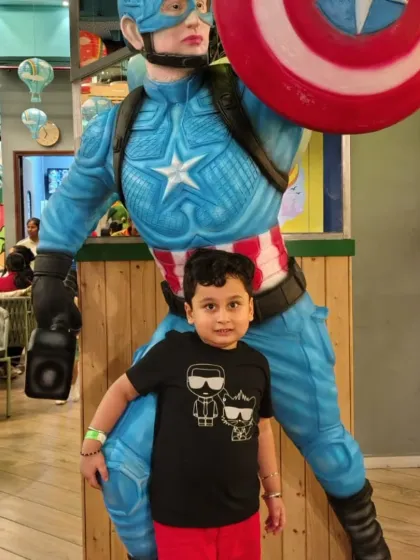 A young fan stands proudly next to the Captain America statue in our cafe area.