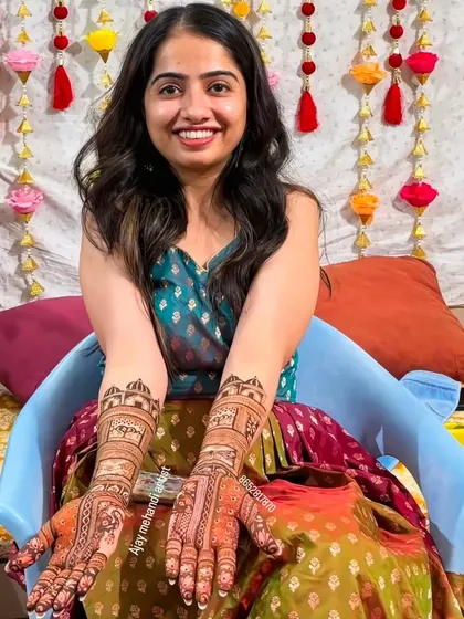 A smiling client displaying her matching bridal mehndi designs, which feature palace architecture at the top.