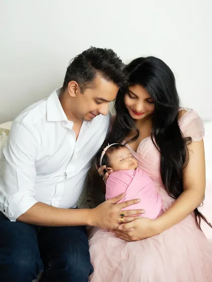 A tender moment with the family seated together, admiring their sleeping baby. The mother's pink dress coordinates beautifully with the baby's swaddle.