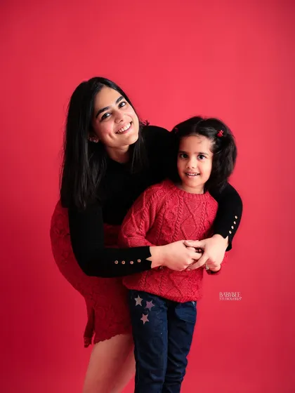 A mother and daughter duo against a vibrant red backdrop. This portrait is full of warmth and happiness, highlighting their cheerful connection.