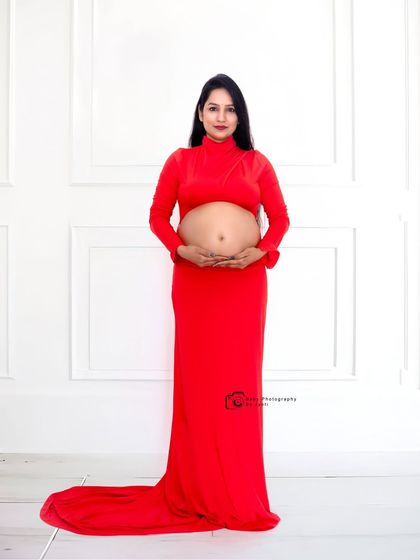 A full-length portrait in a striking red cutout gown against a clean white wall, creating a powerful and modern maternity photo.