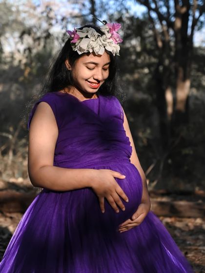 A close-up shot showcasing the beautiful draping on this purple maternity gown. The soft fabric and floral crown create a gentle, bohemian vibe for this happy mother-to-be.