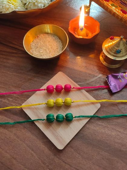 A set of colorful thread-bead rakhis. These are available in bright pink, yellow, and green, perfect for a festive celebration.