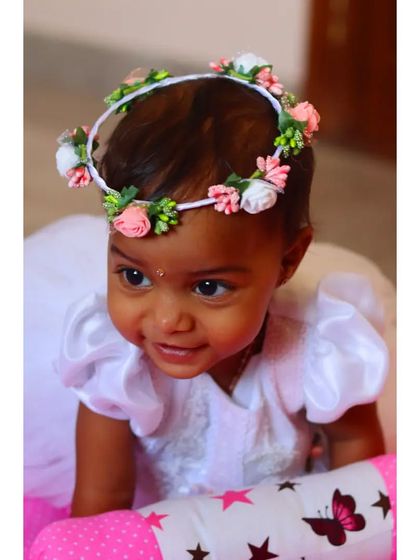 The sweet smile of a baby girl wearing a delicate flower crown. This close-up shot captures her joyful expression and the charming details of her angelic white dress.