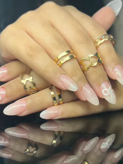 A full view of the long, elegant almond nails with a French ombre base and delicate white bow art.