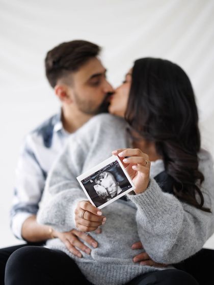 A deeply intimate and romantic moment, with the couple sharing a kiss while holding their baby's first picture.