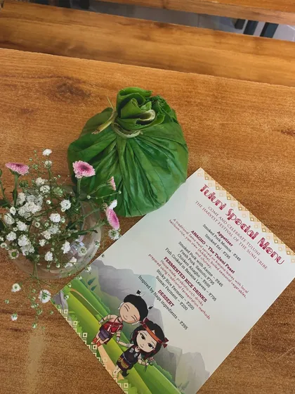 Our special menu for the Tuluni festival, placed next to a traditionally wrapped parcel of food. Every detail is designed to create an authentic experience.