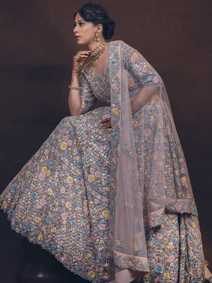 A seated pose that elegantly displays the volume and detailed embroidery of a pastel floral lehenga. The soft lighting and composition create a look of serene sophistication for this bridal piece.