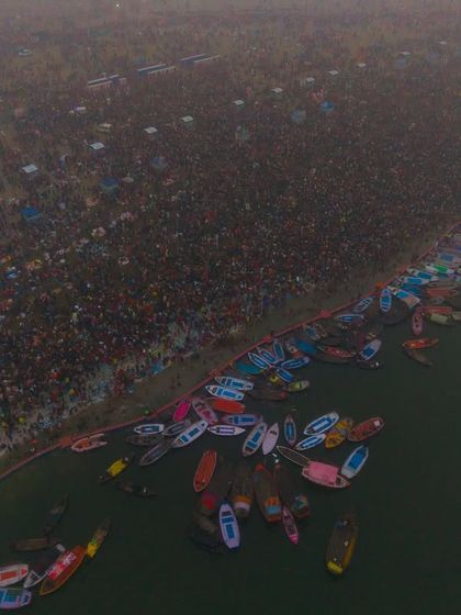 A wider aerial view showing the scale of the crowd along the river during the Kumbh Mela. It gives a sense of the vastness of the event, stretching as far as the eye can see.