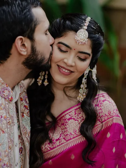 A sweet kiss from the groom during the Haldi ceremony. The bride's makeup looks flawless and romantic.