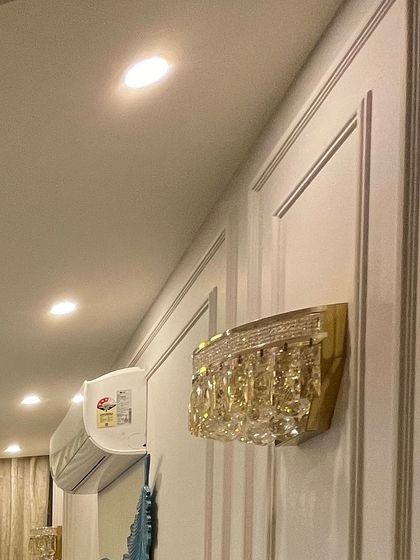 A close-up of a crystal wall sconce mounted on the wainscoting panel. This pairing of classic moulding with a glamorous light fixture is a hallmark of our luxe designs.