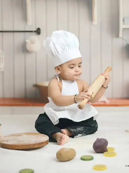 This little baker is hard at work during his first birthday photoshoot. The miniature kitchen set includes a chalkboard, utensils, and play food for a realistic and fun experience.