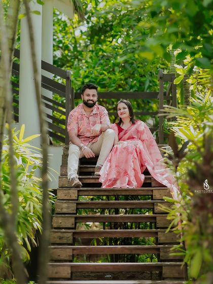 A wider shot of the couple on the wooden staircase, showing the beautiful architecture and greenery of the resort setting.